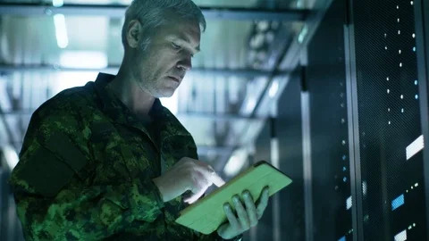 Military Man in Data Center Uses Tablet Computer. Rows of Server Racks are Seen. Stock Footage 74630837