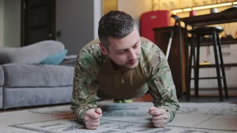 A military man performs a plank exercise on a rug at home. A sofa and kitchen Stock Footage 326369786
