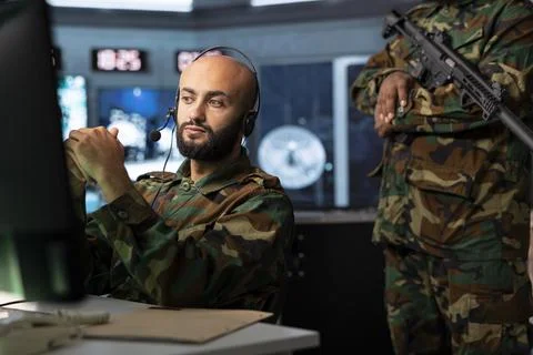 Military operator using headset next to armed security soldier Stock Photos