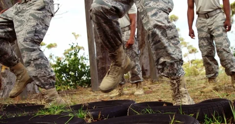 Military troops running over tyres during obstacle course 4k Stock Footage