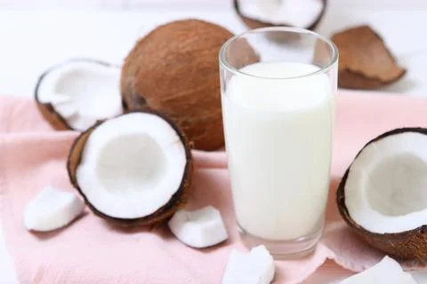 Milk and broken coconuts on the table. Vegetable milk, a veggie drink. Stock Photos