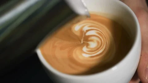 Milk being poured into a mug with coffee, creating a pretty latte art. Vídeo Stock 334648459