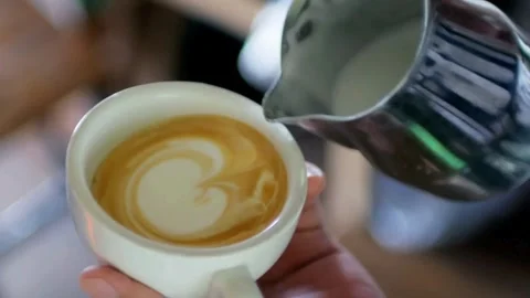 Milk being poured into a mug with coffee, creating a pretty latte art. Stock-Footage 334648530