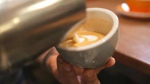 Milk being poured into a mug with coffee, creating a pretty latte art. Stock-Footage 334648570