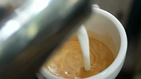 Milk being poured into a mug with coffee, creating a pretty latte art. Stock-Footage 334648581