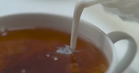Milk being poured in tea, in a white tea cup. Close up in slow motion with a sha Stock Footage 199458742