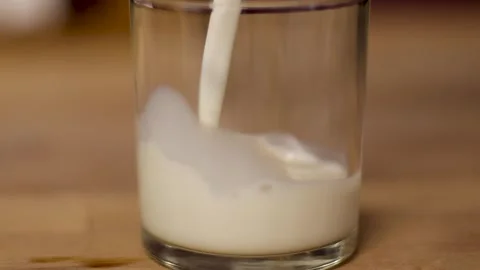 Milk being slowely poured into a glass tumber Stock Footage 245515341