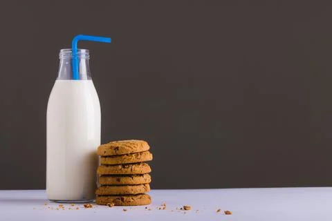 Milk bottle with straw by stack of cookies against gray background, copy space Stock Photos