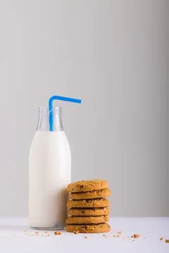 Milk bottle with straw by stack of cookies against white background, copy space 스톡 사진