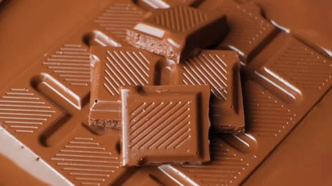 Milk chocolate bars and squares rotating in smooth melted chocolate pool Video stock 346619086