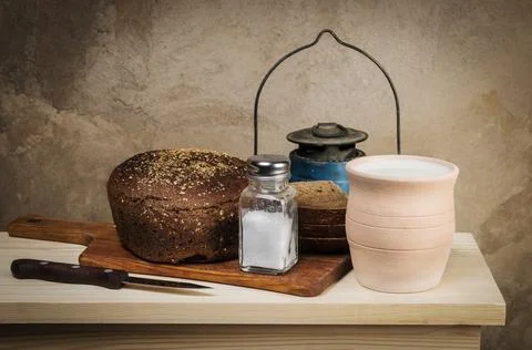 Milk in a clay pot, rye bread, salt in a salt shaker on a cutting board Stock Photos
