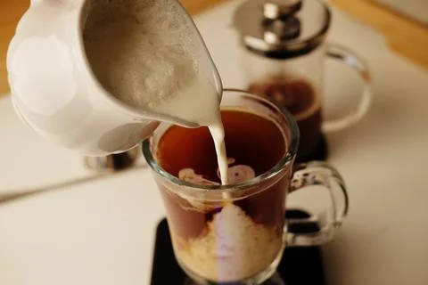Milk coffee preparation process. Lightly whipped cream is poured into the cof Stock Photos