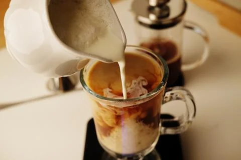 Milk coffee preparation process. Lightly whipped cream is poured into the cof Stock Photos