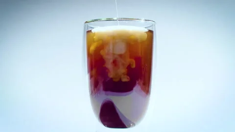 Milk dissolves in coffee or black tea drink. glass with double walls on white Stock Footage 161189441