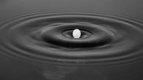Milk drop just about to drop into water, set against dark gray background. Stock Photos