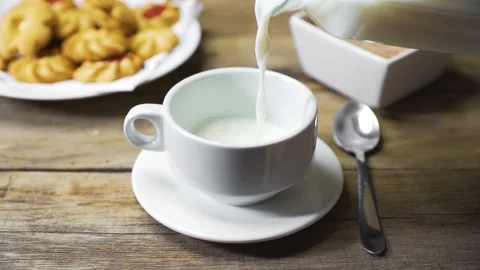 Milk falling in slow motion into white cup on rustic table Stock Footage 143528278