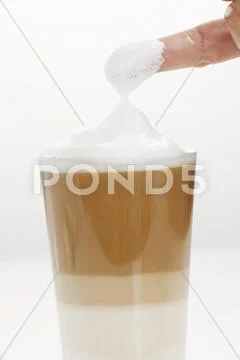 Milk foam covered finger from a glass of Latte Macchiato Stock Photos