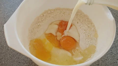 Milk getting poured into a white mixing bowl with cracked eggs and flour in it Stock Footage 168901375