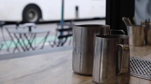 Milk pitcher jugs for coffee making placed on a cafe shop counter against street Vídeos de archivo 244142930