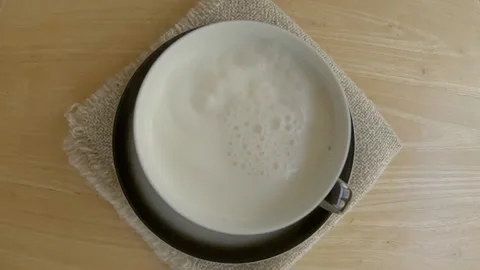 Milk is poured into a cup on a black background, slow motion, top view. Stock Footage 236009868