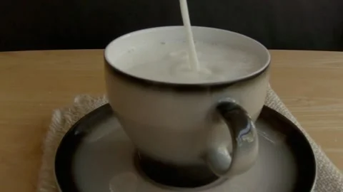 Milk is poured into a cup on a black background, slow motion. Video stock 236009998