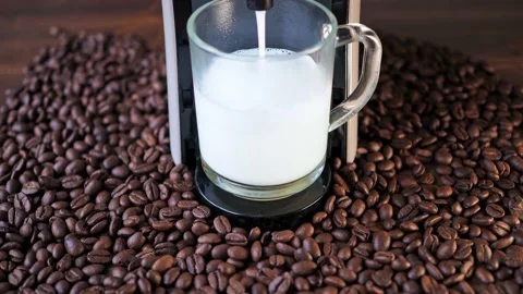 Milk is poured into a cup from a coffee machine. there are coffee beans on the Stock Footage 166524199