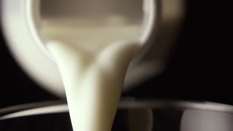 Milk is poured into a glass from a bottle on a black background, close-up, slow Stock Footage