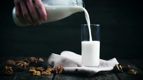 The milk is poured into a glass with walnuts on rustic old wooden table. Stock Footage 86450019