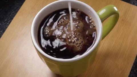 Milk Pouring Into Black Coffee Inside Ceramic Mug Creating Swirling Pattern Video stock 340806398