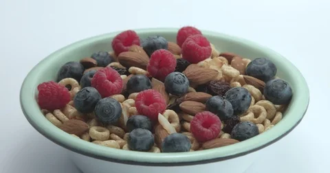 Milk pouring to the bowl with corn flakes rings with berries and nuts. Video stock 76996485