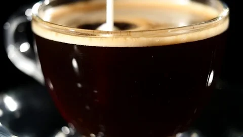 Milk pouring into coffee in a glass in slow motion Stock Footage