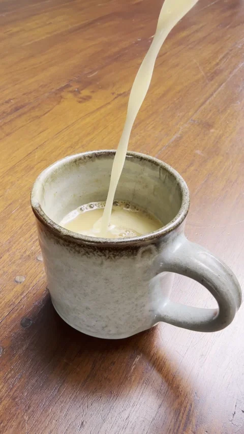 Milk Pouring Into Coffee in Rustic Ceramic Mug on Wooden Table Stock Footage 348587101