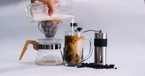 Milk pouring into cold brew iced coffee glass on table with coffee drip object Stock Footage 142741298