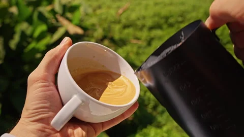Milk Pouring Into Fresh Coffee Creating Latte Art Pattern in White Cup Held in H Stock Footage 330133604