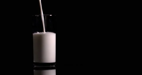Milk is pouring into a glassful on a black background Stock Footage