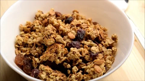 Milk pouring onto muesli cranberry crunchy cereal in a bowl on breakfast table  Stock Footage