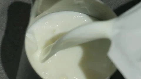 Milk pours into partially filled pitcher creating whirls Video stock 317087174