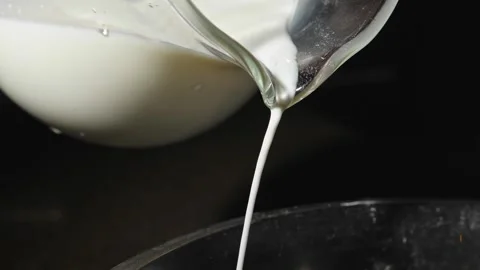 Milk pours in a thin trickle from a glass jug against a dark background, close Stock Footage 264415544