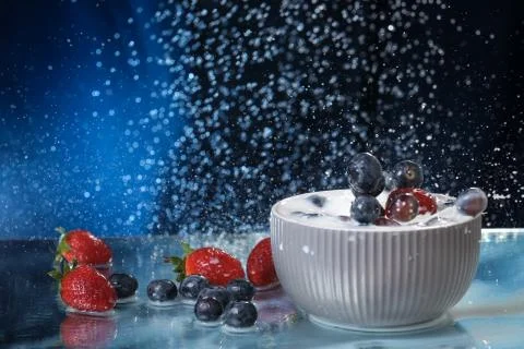 Milk splash close up of falling berries in a grey plate of milk. Stock Photos