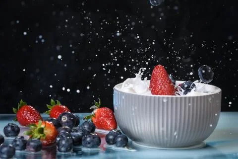 Milk splash close up of falling berries in a grey plate of milk. Stock Photos