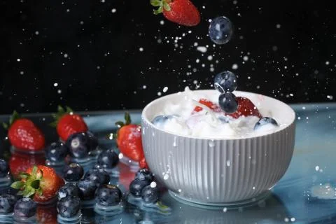 Milk splash close up of falling berries in a grey plate of milk. Stock Photos