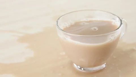 Milk Tea Splashing and Spilling from Glass Cup on Wooden Table Stock Footage 345767940