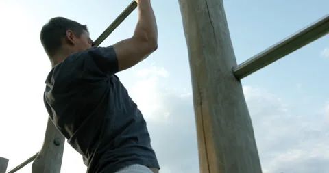 Millenial man doing pull up on at an outdoor gym. 库存影片 130217861