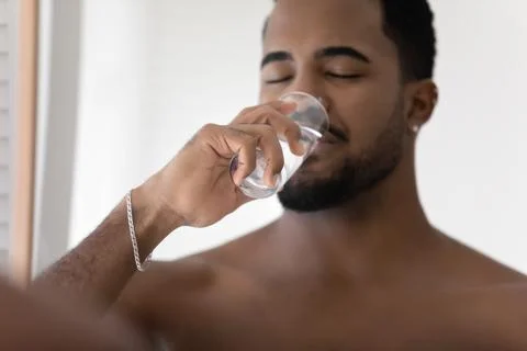 Millennial African man drinking pure clean mineral water indoors Stock Photos