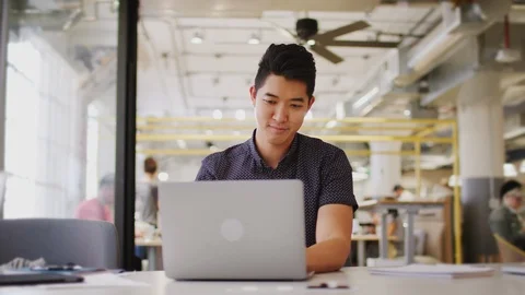 Millennial Asian man using laptop computer sitting at a table in an office Stock-Footage 106697365