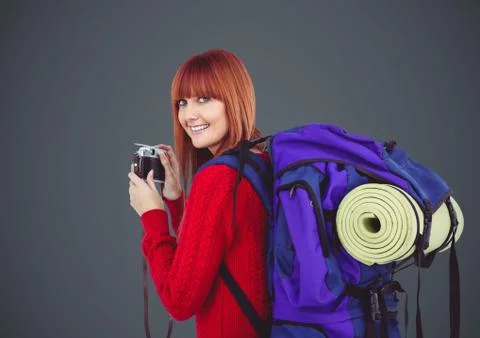 Millennial backpacker with camera against grey background Stock Photos