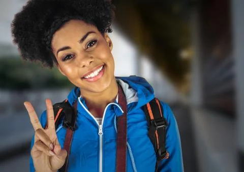 Millennial backpacker making peace sign against blurry train station Stock Photos