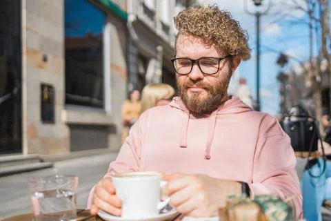 Millennial bearded man having breakfast at table of street cafe on spring day Foto stock