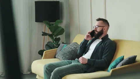 Millennial bearded man sitting on couch at home chatting, typing message using Stock Footage 154905191
