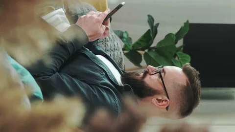 Millennial bearded man sitting on couch at home chatting, typing message using Stock Footage 155404893